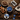 Assorted dark chocolate squares, cocoa beans, chopped chocolate, and nuts are arranged on a rustic wooden table with blue-wrapped chocolates in bowls and plates, alongside a linen napkin and wooden utensils.