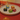 Five individually wrapped chocolates in colorful foil—black, blue, orange, green, and pink—are arranged on a white plate with a gold rim, set on a red tablecloth.