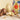 Several colorful boxes and assorted chocolate Easter eggs, some whole and some broken open, are displayed on a beige surface with scattered nuts and chocolate pieces.