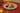 A white plate with a gold rim holds five individually wrapped chocolates in colorful foil (blue, green, gold, pink, and black), set on a red tablecloth with candles and glasses in the background. - AI generated text